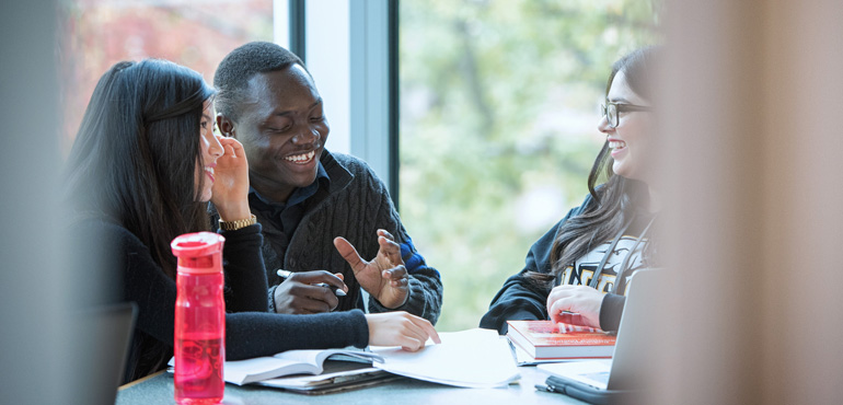 Three students sit at a table, talking and laughing