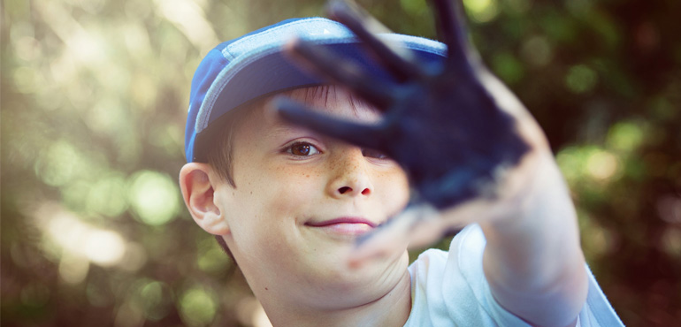 A child faces the camera, showing off a hand covered in blue paint