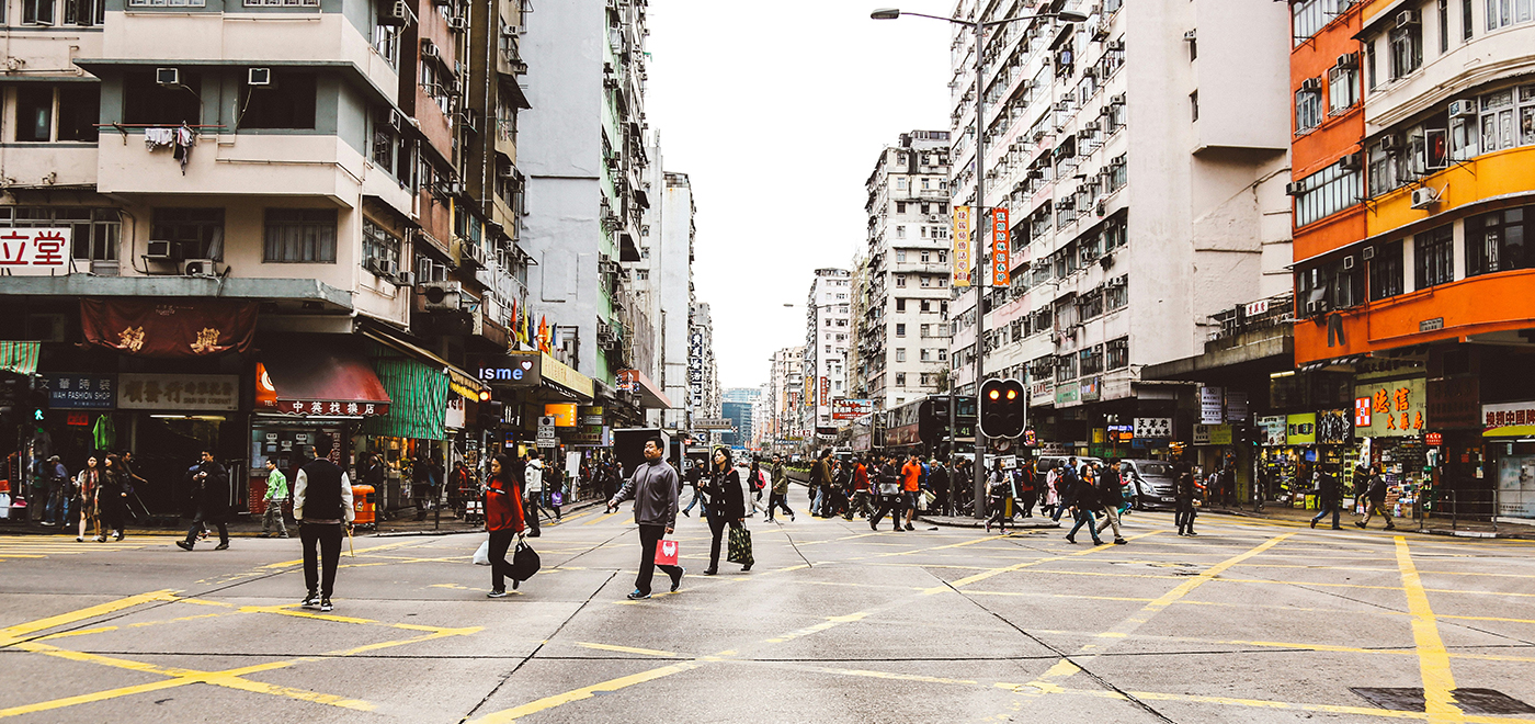 An urban intersection, with pedestrians crossing the street in the foreground and buildings in the background. Photo by Alex Wong on Unsplash