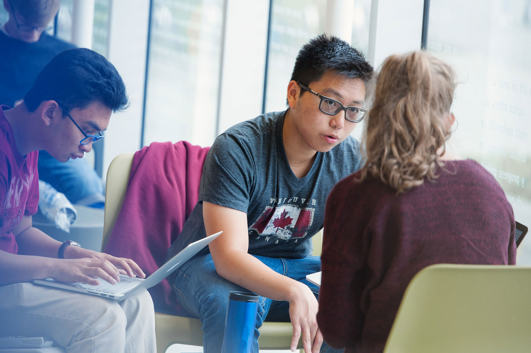 Three students holding a conversation over laptops, in the UBC Bookstore.